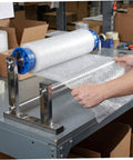 Manual Stretch Film Dispenser Stand For Shipping Supplies Hand Operated Wrap Film Holder With Metal And Plastic Construction Lightweight Yet Sturdy For Easy Desktop Wrapping And Efficient Warehouse Or Home Packing. Bubble wrap roll on metal stand used for packing