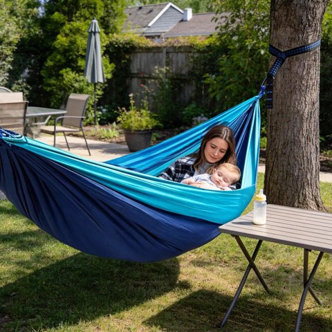 Woman with baby relaxing in Single Portable Parachute Nylon Hammock For Outdoor Adventure, tied to a tree, in backyard setting.