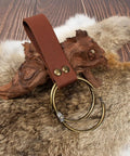 Solid leather strap with brass ring on a fur background, part of Snag This Solid Leather Waist Bag And Fanny Pack With Durable Adjustable Belt Strap Badass Steampunk Style Ideal For Festival Cosplay And Mobile Device Storage.
