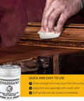 Person applying Micro Crystalline Wax Polish for Furniture, Wood, Leather and Metal on a wooden surface with a cloth.