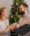 Couple exchanging gifts in front of decorated Christmas tree with exquisite gift box visible