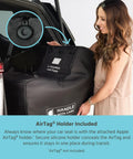 Woman placing Fully Padded Infant Car Seat Travel Bag For Airplane Trips Fits Most Car Seats Gate Check Ready AirTag Compatible Durable Black Cover For UPPAbaby Nuna Chicco And More into a vehicle trunk