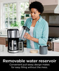 Woman filling 60 oz water reservoir of 12 Cup Programmable Coffee Brewer With Classic Or Rich Brew Styles, Black Stainless Finish.