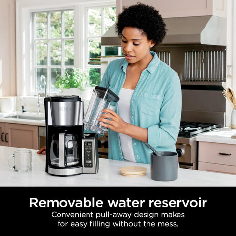 Woman filling 60 oz water reservoir of 12 Cup Programmable Coffee Brewer With Classic Or Rich Brew Styles, Black Stainless Finish.
