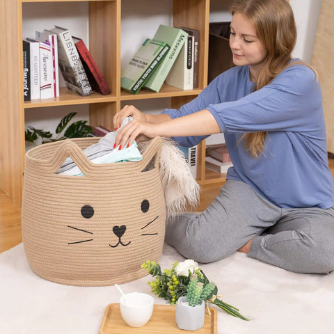 Person placing items in Large Cotton Rope Storage Basket With Cozy Cat Face Design For Towels, Blankets, Toys, and Clothes, 15x14 inches
