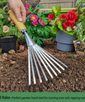 Stainless Steel Hand Rake With Ergonomic Handle For Gardening in use for cultivating soil in flower bed, surrounded by plants