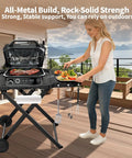 Heavy Duty Foldable Outdoor Grill Stand With Wide Ninja Woodfire And Blackstone Compatibility on a patio, woman placing food.