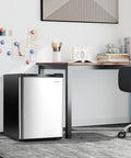 Compact Upright Freezer Featuring Tunable Thermostat And Snap Out Shelves under desk in sleek silver design.