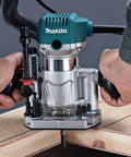 Close-up of a person using the Beefy One And One Quarter Horsepower Compact Router Kit With Variable Speed From 10000 To 30000 RPM Rack And Pinion Fine Depth Adjustment Slim Ergonomic Body And Quick Release Cam Lock For Precise Comfortable Woodworking on a wooden surface.