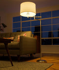Theta Swing Arm Floor Lamp With Brushed Steel Finish placed beside a sofa in a living room, illuminating with its drum shade.