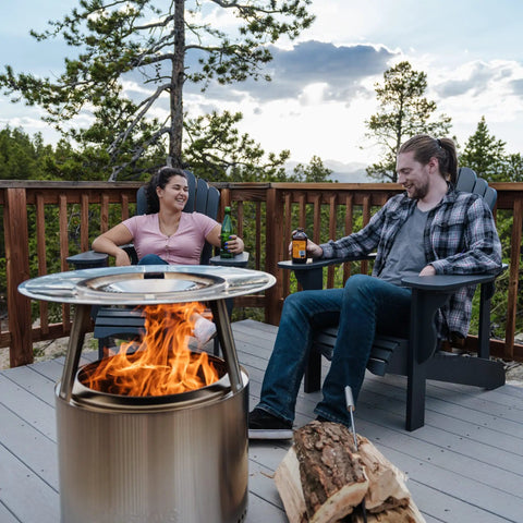 Ranger Heat Deflector Boosts Outdoor Fire Pit Warmth With Angled Design visible in use on a deck with two people enjoying the fire