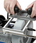 Close-up of Universal Molding Knife Sharpener Attachment for European Pin Style Blades on Tormek sharpener with hands aligning blade.