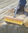 Long Handled Floor Scrubber Brush With 52 Inch Reach for Decks, wooden handle and stiff bristles scrubbing a wooden deck surface.