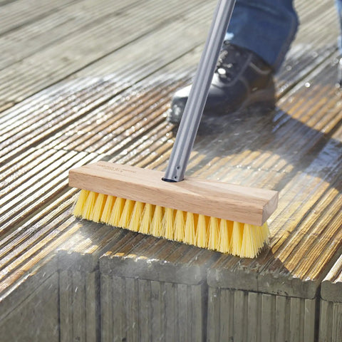 Long Handled Floor Scrubber Brush With 52 Inch Reach for Decks, wooden handle and stiff bristles scrubbing a wooden deck surface.