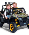 Two children seated in a camo-patterned ride-on toy resembling a John Deere Gator XUV and Polaris RZR 900 model.