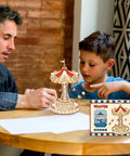 Father and son assembling 3D Wooden Puzzle Music Box Kit With Led Rotating Swing Ride on table, box shown on side.