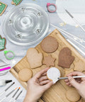 Badass 112 Piece Baking Decorating Kit With Sturdy Acrylic Turntable and decorated cookies on a wooden board.