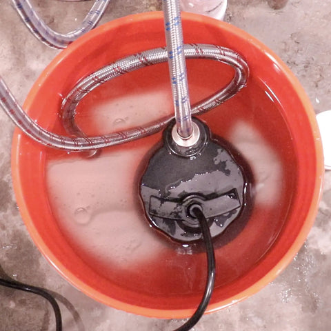 Tankless Water Heater Descaling Flush Kit with heavy duty pump and steel hoses submerged in 3.5 gallon bucket for cleaning.