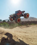 Quake GROM 4x4 RC Monster Truck One Sixteenth Scale jumping over dirt mound outdoors in red with high traction drivetrain