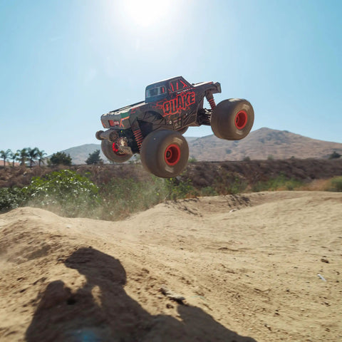 Quake GROM 4x4 RC Monster Truck One Sixteenth Scale jumping over dirt mound outdoors in red with high traction drivetrain