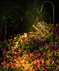 Copper Solar Watering Can Garden Light With Waterfall Effect And 60 LEDs illuminating colorful flowers at night.