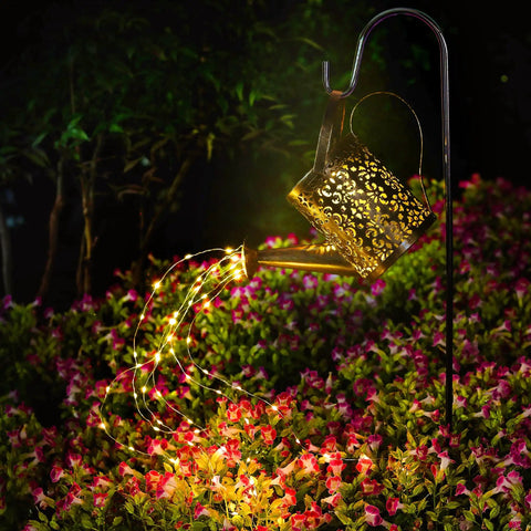 Copper Solar Watering Can Garden Light With Waterfall Effect And 60 LEDs illuminating colorful flowers at night.