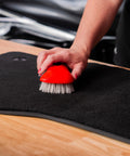 Person using stiff bristle carpet and upholstery scrub brush for auto and home use, heavy duty grime buster on carpet mat.