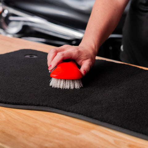 Person using stiff bristle carpet and upholstery scrub brush for auto and home use, heavy duty grime buster on carpet mat.