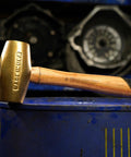 Non Sparking Brass Hammer 18 Inch 5 Pound USA Made With Wood Handle And Double Faced Head, resting on a blue barrel.