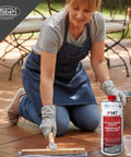 A woman applying Hella Strong Solvent Based Color Enhancing Stone Sealer on patio tiles, clear one-liter bottle beside her.