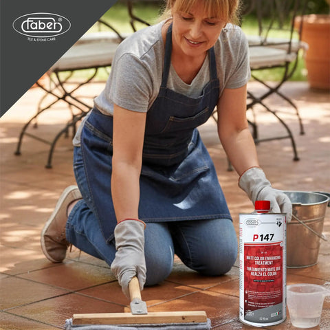 A woman applying Hella Strong Solvent Based Color Enhancing Stone Sealer on patio tiles, clear one-liter bottle beside her.