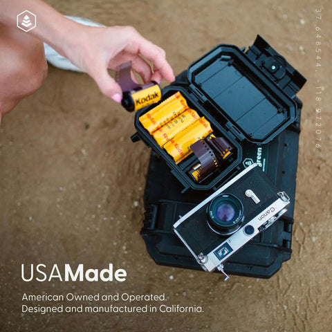 Badass Mil Spec Waterproof Dry Box Case For Cameras Camping And Survival Gear IP67 with film rolls and a camera on a sand surface.
