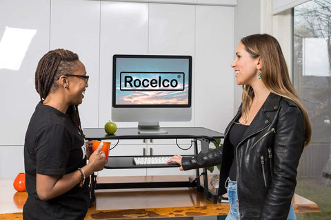 32 Inch Height Adjustable Standing Desk Converter With Slide Out Keyboard Tray and Dual Monitor Riser, two women using it in a bright office.