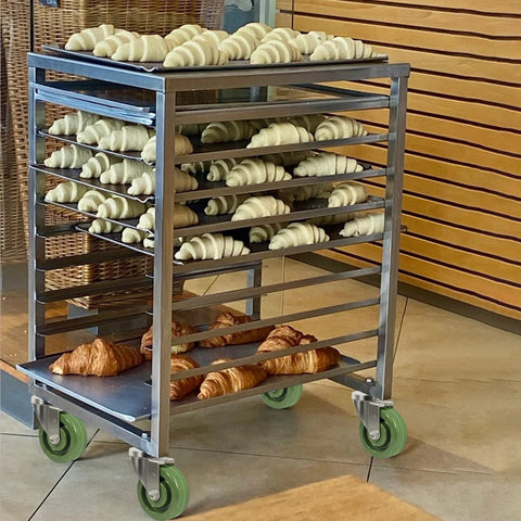 Front view of stainless steel rolling bakery rack on four green 4-inch caster wheels with croissants