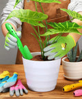 Child using 24 Piece Kid Friendly Garden Tool Set With Mini Colorful Metal Shovels And Gloves Includes 12 Hand Trowels In 6 Colors And 12 Pairs Of Garden Gloves Ideal For Little Gardeners 11 By 3 Inch Shovels to plant in a white pot