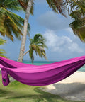 Double Camping Hammock With Ropes For Two People, Ultra Lightweight Portable Gear, 210T Nylon Parachute Fabric, Fuchsia Pink on a beach.