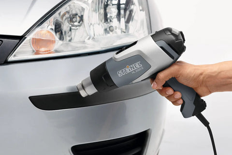 Hand holding HL 2020 E Pro Grade Heat Gun With LCD Display 1600 W Hot Air Tool near car bumper for repair application