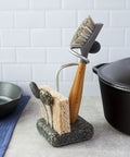 Heavy Granite Base Kitchen Sink Caddy With One Handed Grab And Go Quick Dry Sponge And Brush Holder Eco Friendly Handmade Granite And Aluminum Organizer Handcrafted In New Hampshire Made In USA Stable No Tip, holding a brush and sponge next to a cast iron pot on a kitchen counter.