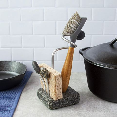 Heavy Granite Base Kitchen Sink Caddy With One Handed Grab And Go Quick Dry Sponge And Brush Holder Eco Friendly Handmade Granite And Aluminum Organizer Handcrafted In New Hampshire Made In USA Stable No Tip, holding a brush and sponge next to a cast iron pot on a kitchen counter.