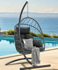 Gray Egg Chair With Stand For Indoor And Outdoor Use, Hanging Rattan Wicker Swing Chair With Cushion by a poolside.