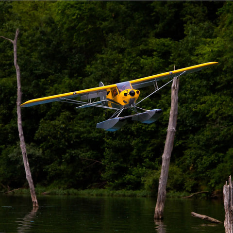 Carbon Cub 15cc ARF Ready To Fly RC Plane With Laser Cut All Wood Construction in flight over water with backdrop of trees.