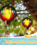 Colorful glass hot air balloon solar lanterns with flickering flame hummingbird design hanging outdoors, lush greenery background.