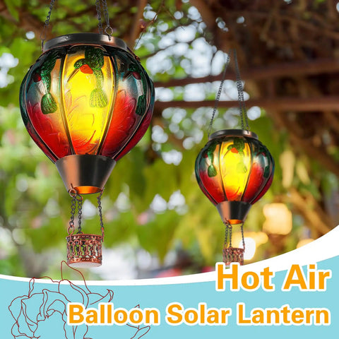 Colorful glass hot air balloon solar lanterns with flickering flame hummingbird design hanging outdoors, lush greenery background.
