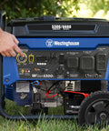 Close-up of Beast 6600 Watt Portable Generator For Home Backup With Remote Start and CO Sensor outdoors on grass, hand on button.