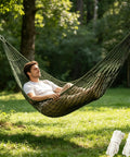 Man relaxing in olive green 98 x 31.5 in breathable mesh hammock with nylon net setup outdoors on trees, 100 kg capacity