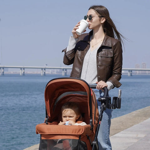 Mother with stroller by water using 2 In 1 Cup Holder Attachment For Q1 Wagon Only, With Secure Grip And Easy Access, in black.