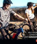 Two people in cycling gear, with mountain bikes in a rugged outdoor setting, showcasing multi-speaker connection feature.