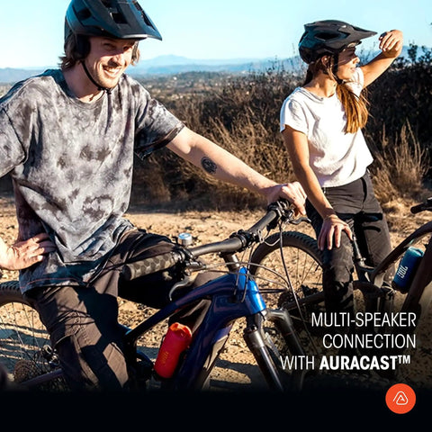 Two people in cycling gear, with mountain bikes in a rugged outdoor setting, showcasing multi-speaker connection feature.