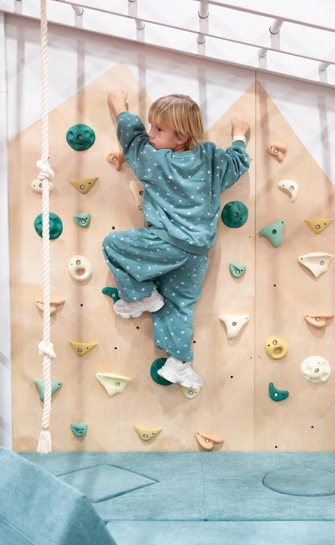 Child climbing on premium Boho rock climbing holds for kids indoor wall set in earth tones with durable wall props for home play.