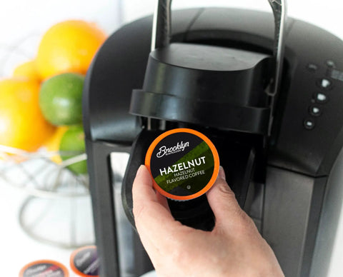 Hand placing Hazelnut pod from Flavored Keurig K Cup Compatible Coffee Pods Flavor Packed Variety Pack 40 Count into brewer